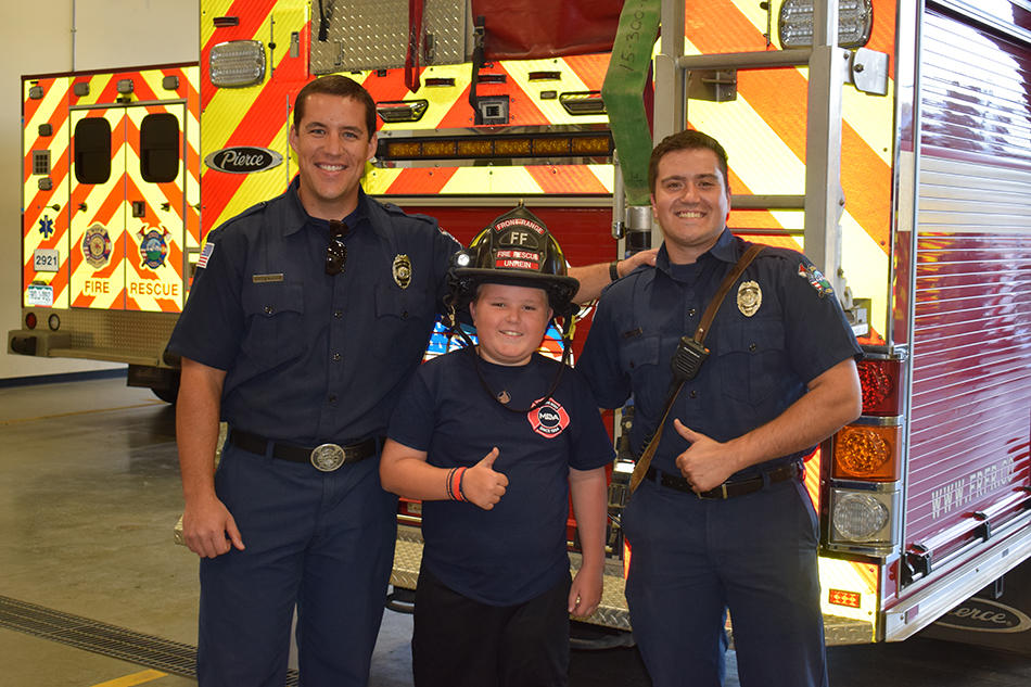 Firefighters and a kid posing in front of a fire truck