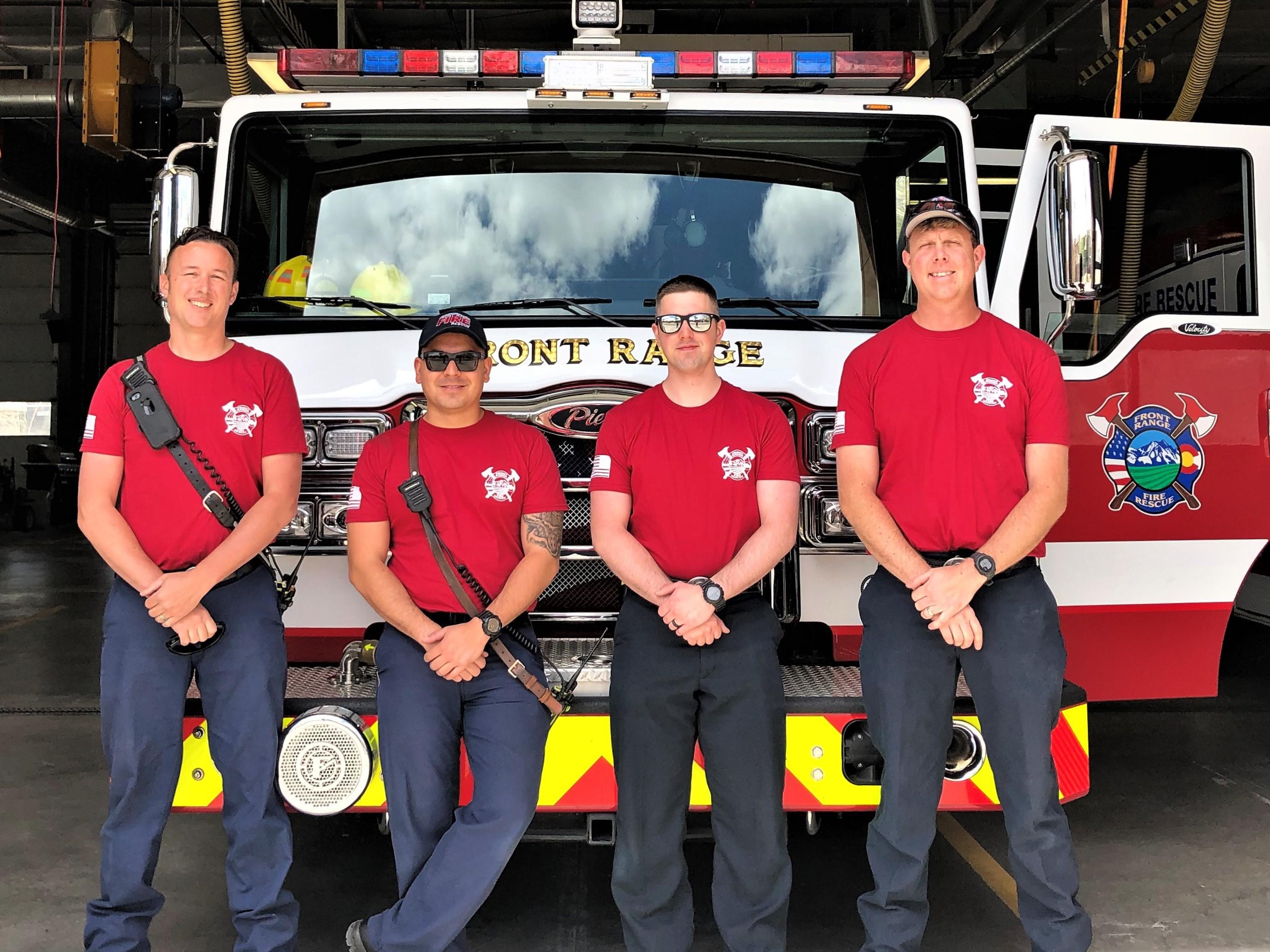Four Firefighters wearing red and standing in front of a firetruck